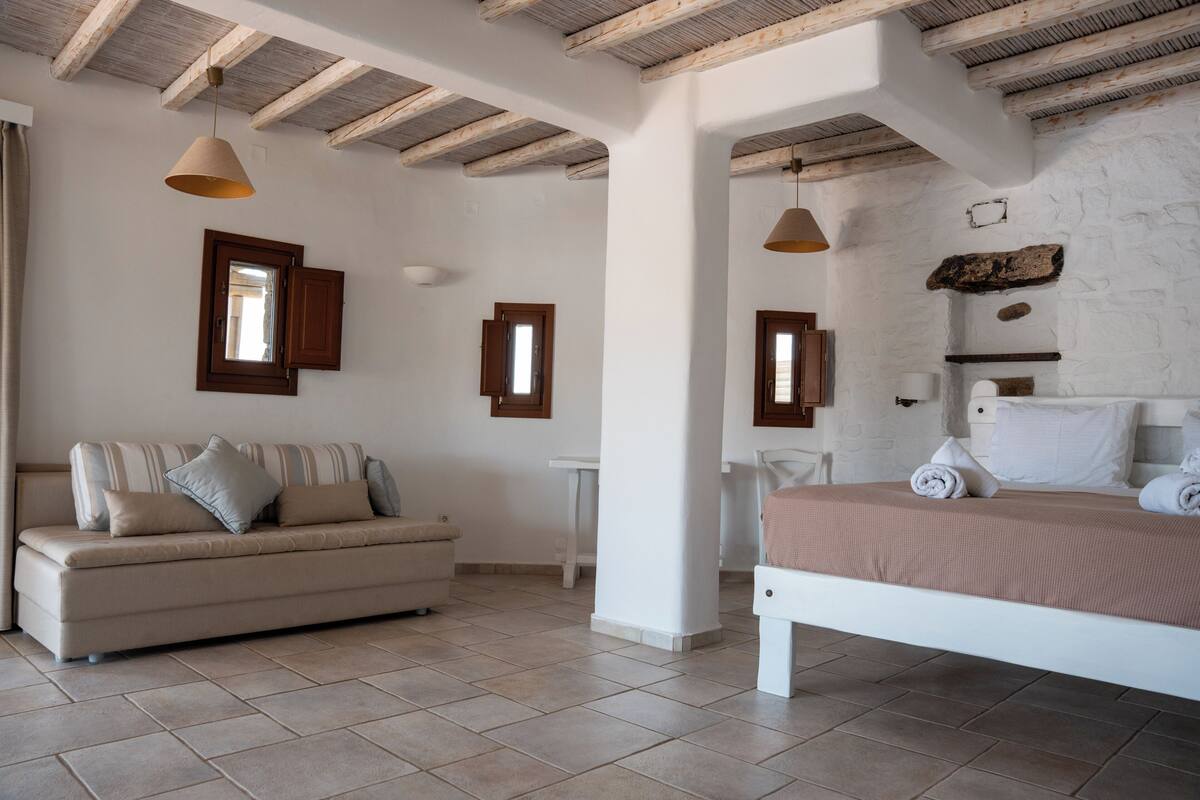 A bedroom with a bed, a sofa, a small table, and a mirror.