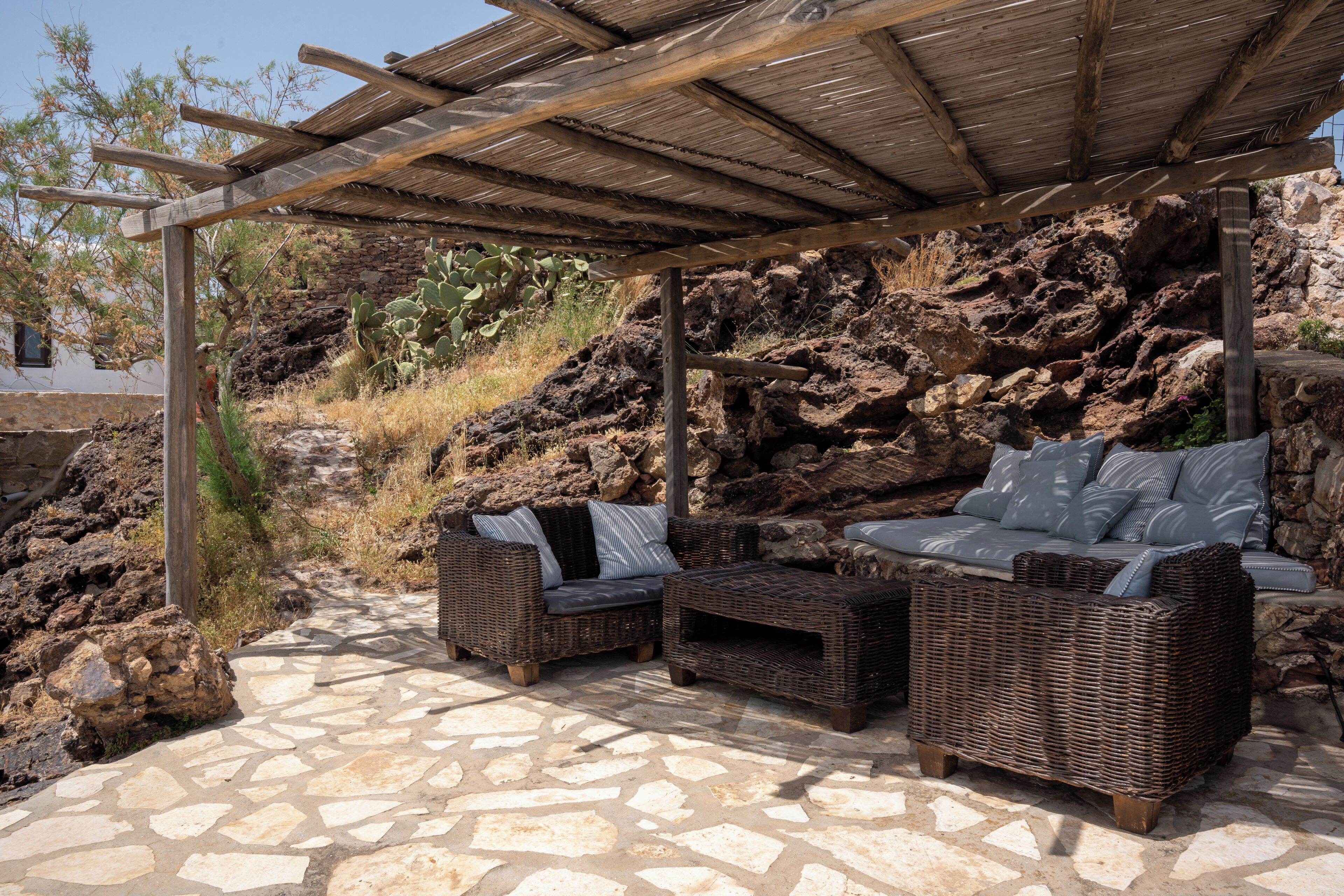 An outdoor seating area with wicker furniture, a stone floor, and a rock wall backdrop.