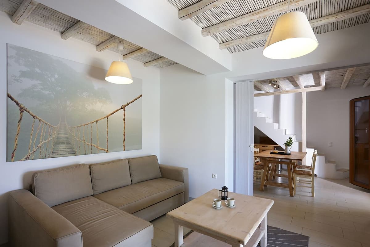 A modern living room with a sofa, a wooden coffee table, and a large painting of a rope bridge. There is a staircase leading to another room.