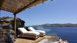 A seaside lounge with two cushioned chairs, a table with drinks, and a clear view of the ocean and distant hills. - Albatros Club Mykonos (Mykonos)