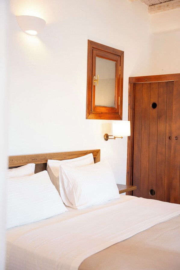 A neatly made bed with white linens in a room with a wooden door and a wall-mounted mirror. - Albatros Club Mykonos (Mykonos)
