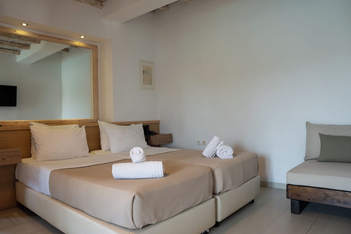 A double bed with two pillows, a bedside table, a flat-screen TV mounted on the wall, and a small bedside table with a lamp.