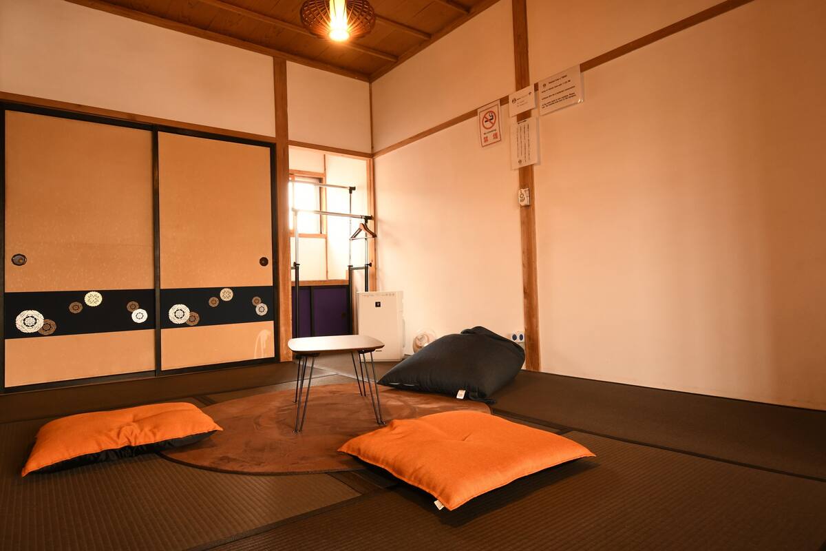A tatami mat room with a low table, two cushions, and a hanging coat rack.