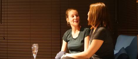 Two people sitting on a blue couch with a wooden table and a glass of water in front of them.