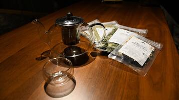 A wooden table with a glass teapot, a glass cup, a black container, and packets of organic orange peel tea.