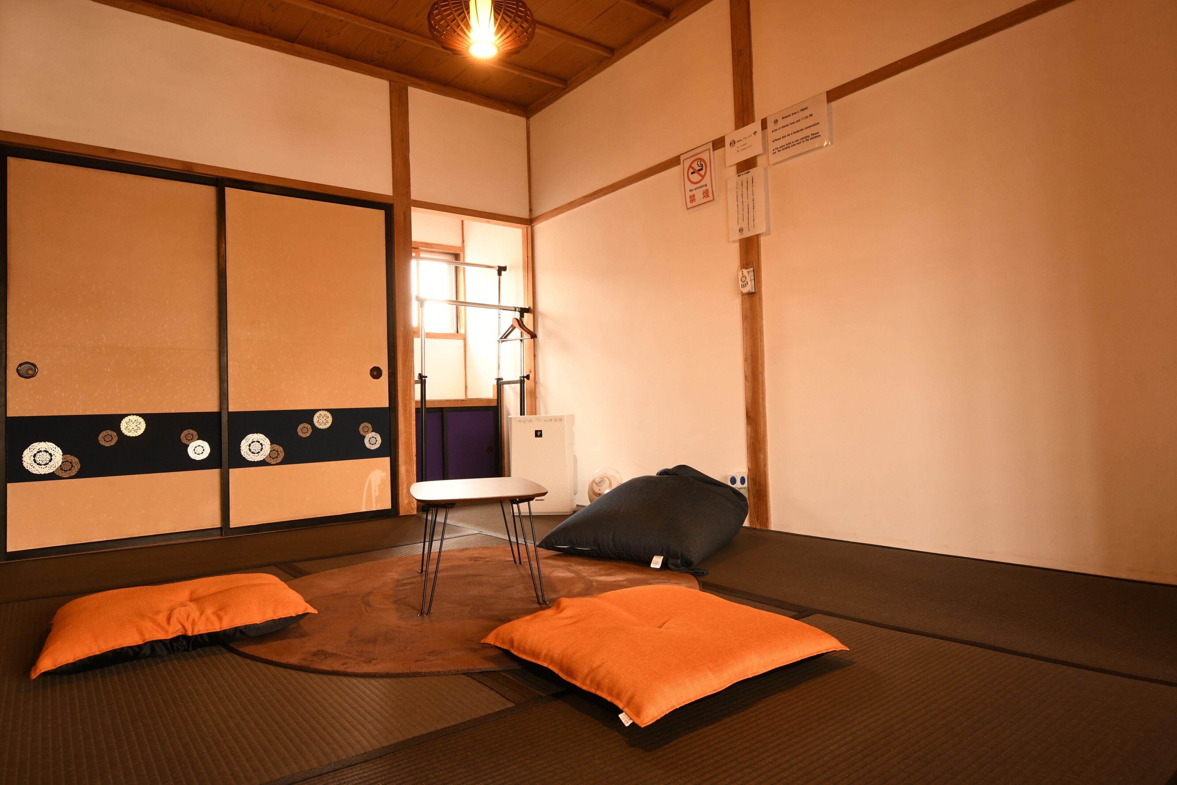 A tatami mat room with a low table, two pillows, a hanging rack, and a sliding door.