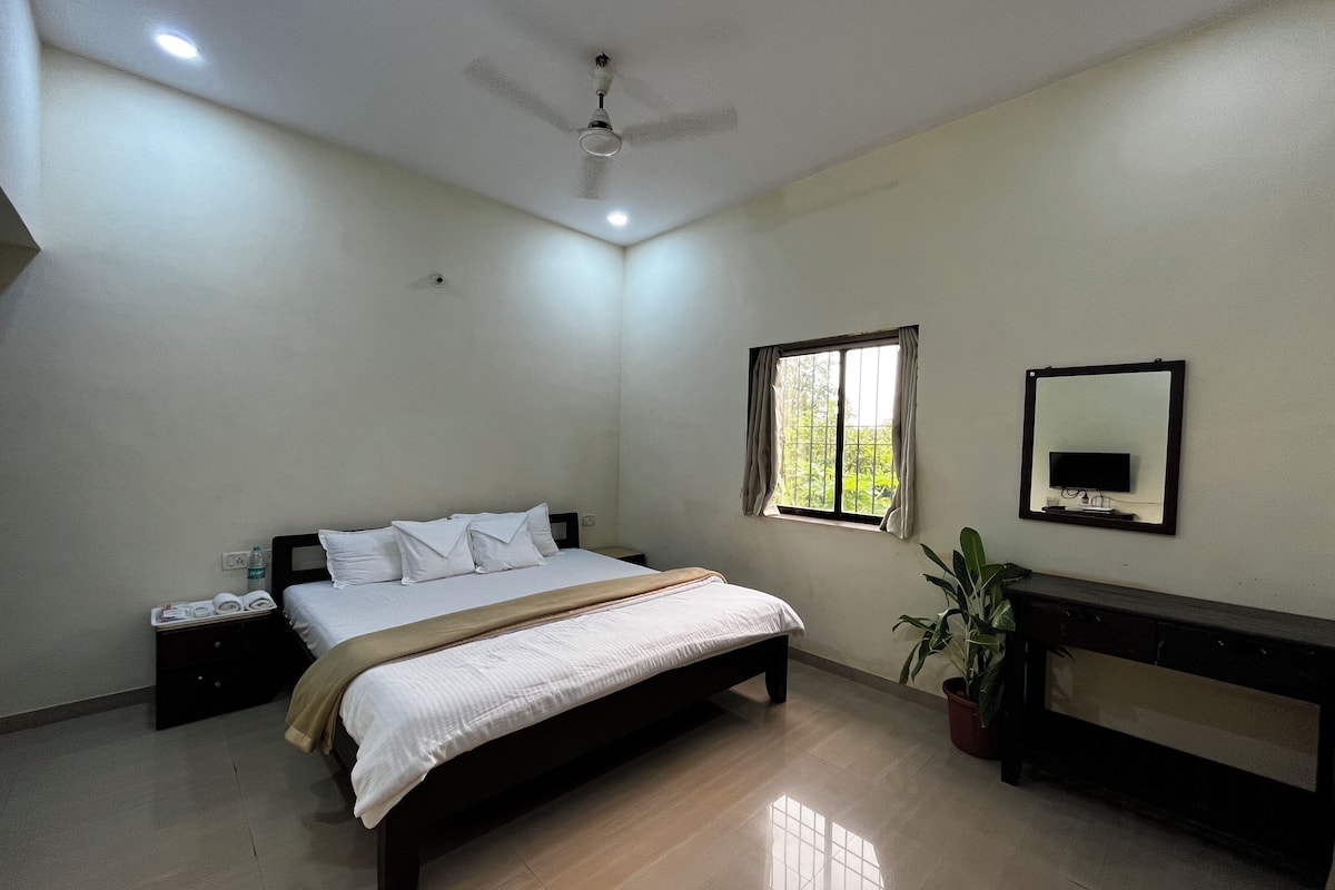 A bedroom with a bed, bedside tables, a ceiling fan, a window, a mirror, and a potted plant.