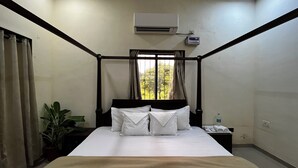 Una cama con dosel, ropa de cama blanca, una mesita de noche con un teléfono y una botella, y una ventana con cortinas.