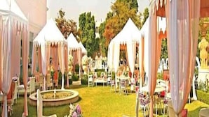 Un jardín al aire libre con carpas blancas, una zona de estar central con un sofá rosa y una fuente.