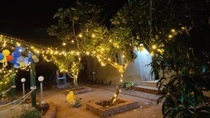 Un espacio al aire libre con luces colgantes, un pequeño árbol y una jardinera de hormigón.