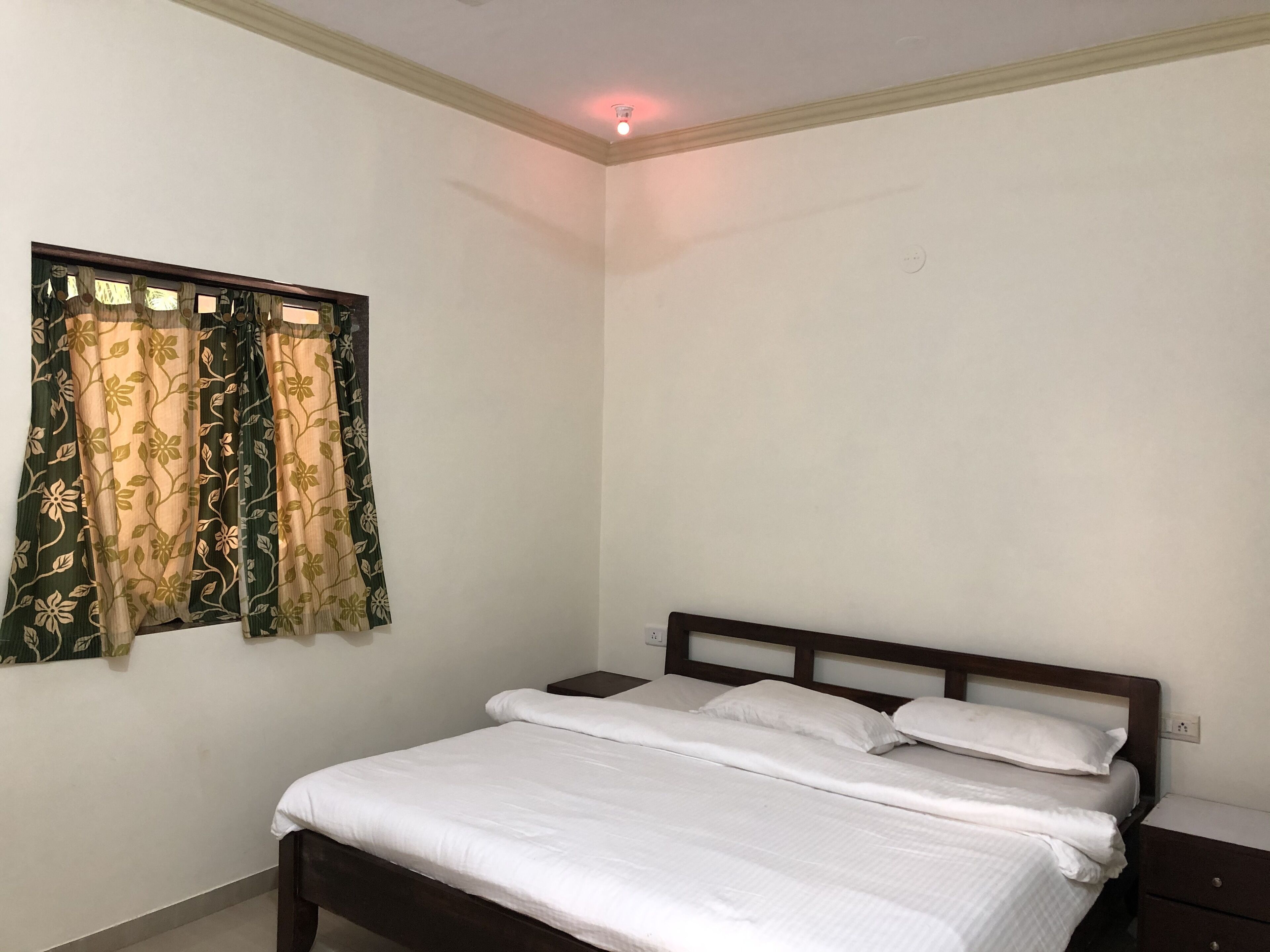 Een slaapkamer met een enkel bed, een nachtkastje en een raam met bloemen gordijnen.