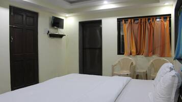 A hotel room with a bed, a TV mounted on the wall, two chairs, and a window with curtains.