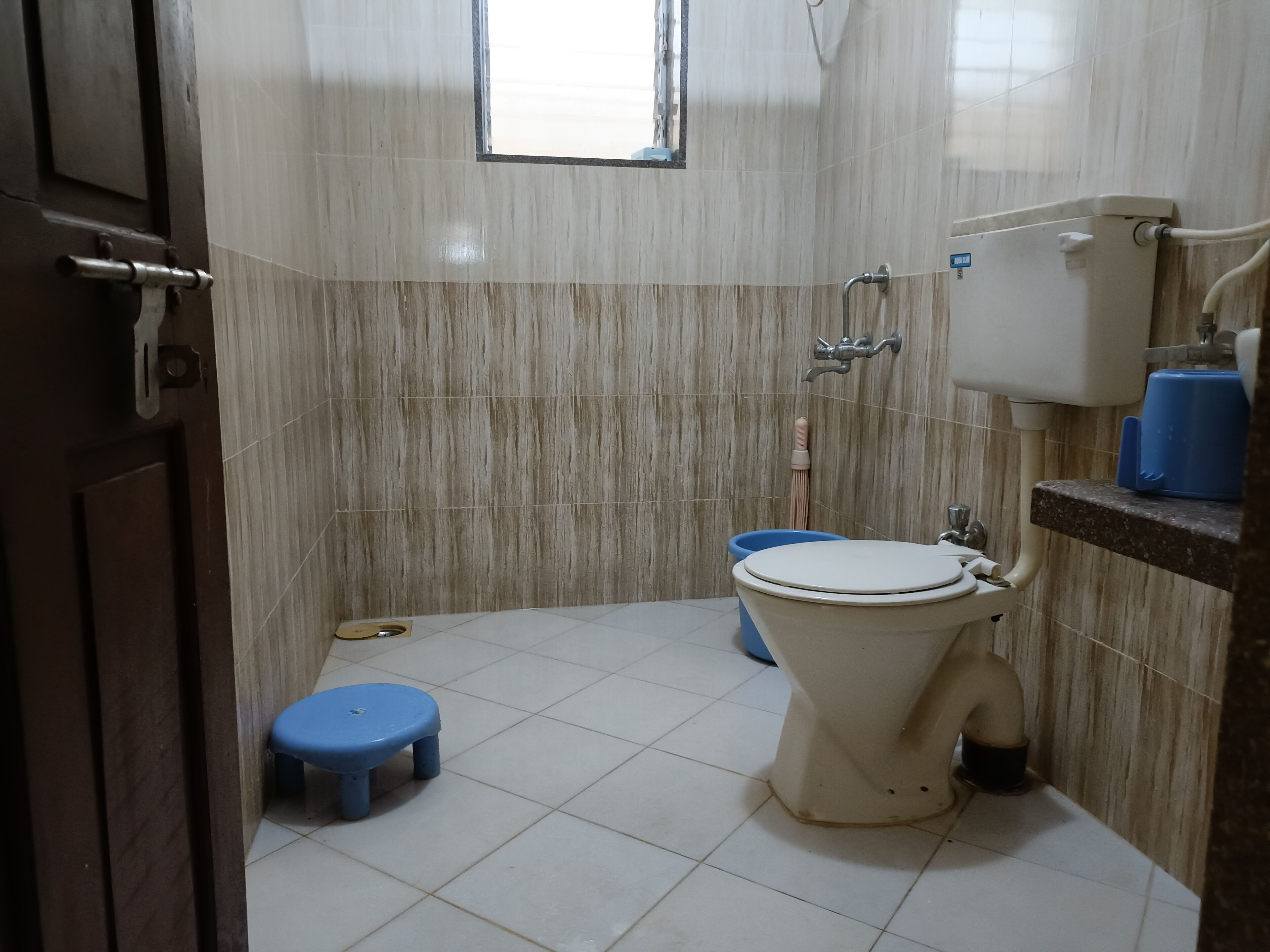 Un baño pequeño con un inodoro, un cubo azul y un taburete azul.