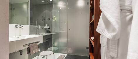 A modern bathroom with a glass-enclosed shower, a vanity with a mirror, and a wooden robe stand.