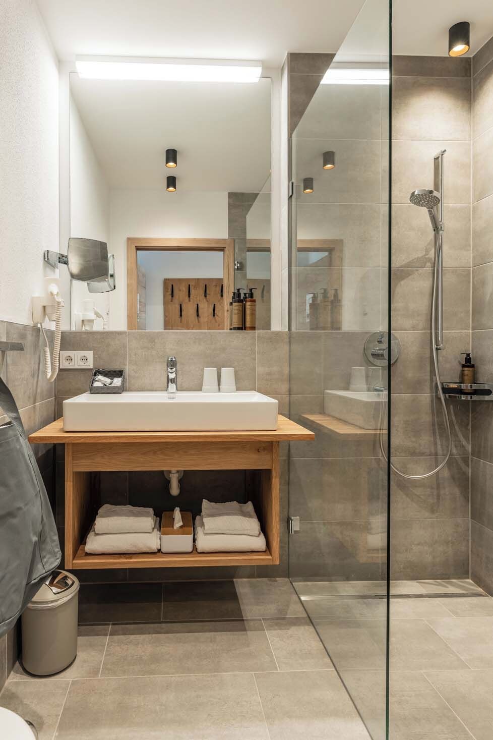 A modern bathroom with a large mirror, a wooden vanity, a glass shower enclosure, and a toilet.