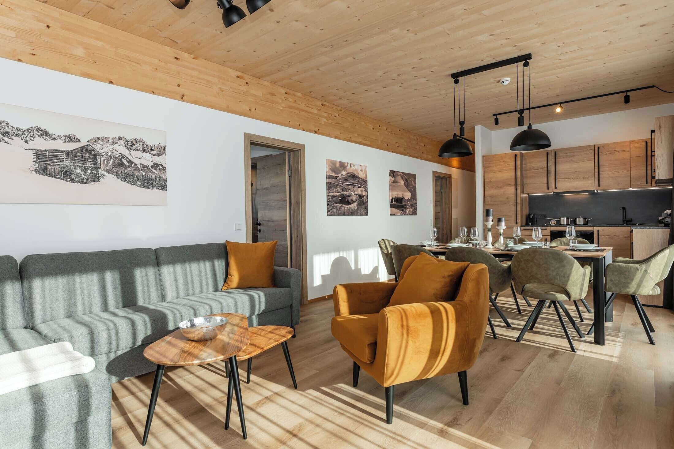Una sala de estar moderna con un sofá, sillones y una mesa de centro. Hay una zona de cocina con armarios de madera y una mesa de comedor.
