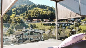 A modern hotel room with a large window offering a view of a hillside village. - AlpenParks Hotel & Apartment Taxacher (Kirchberg in Tirol)