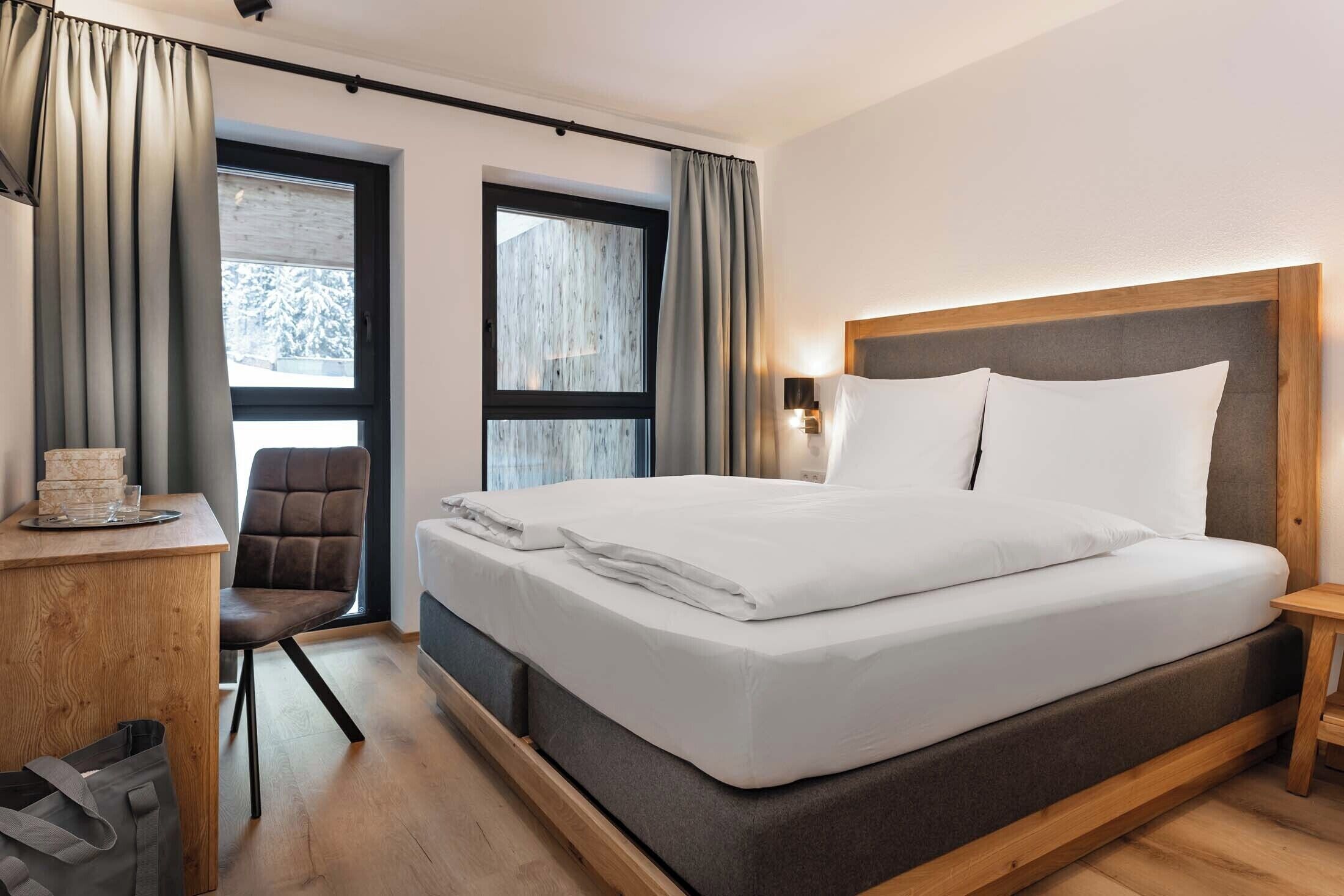 A modern hotel room with a large bed, a desk, and a chair.