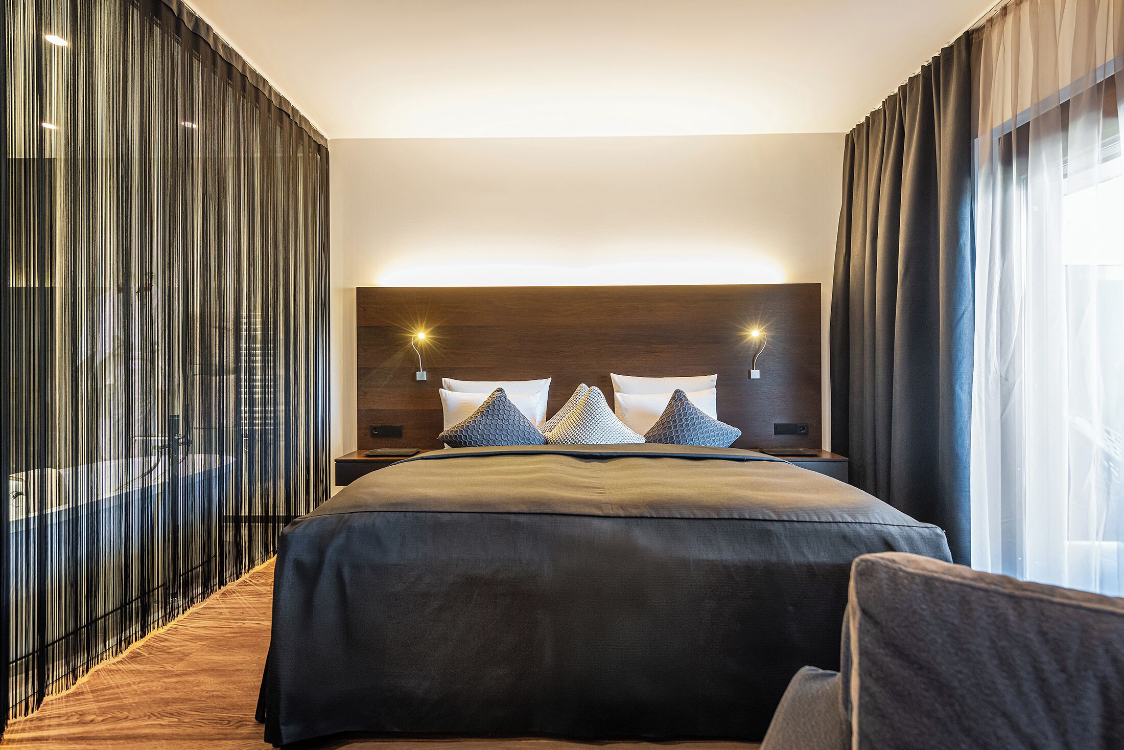 Een moderne hotelkamer met een groot bed, een houten hoofdbord en een glazen scheidingswand aan de zijkant.