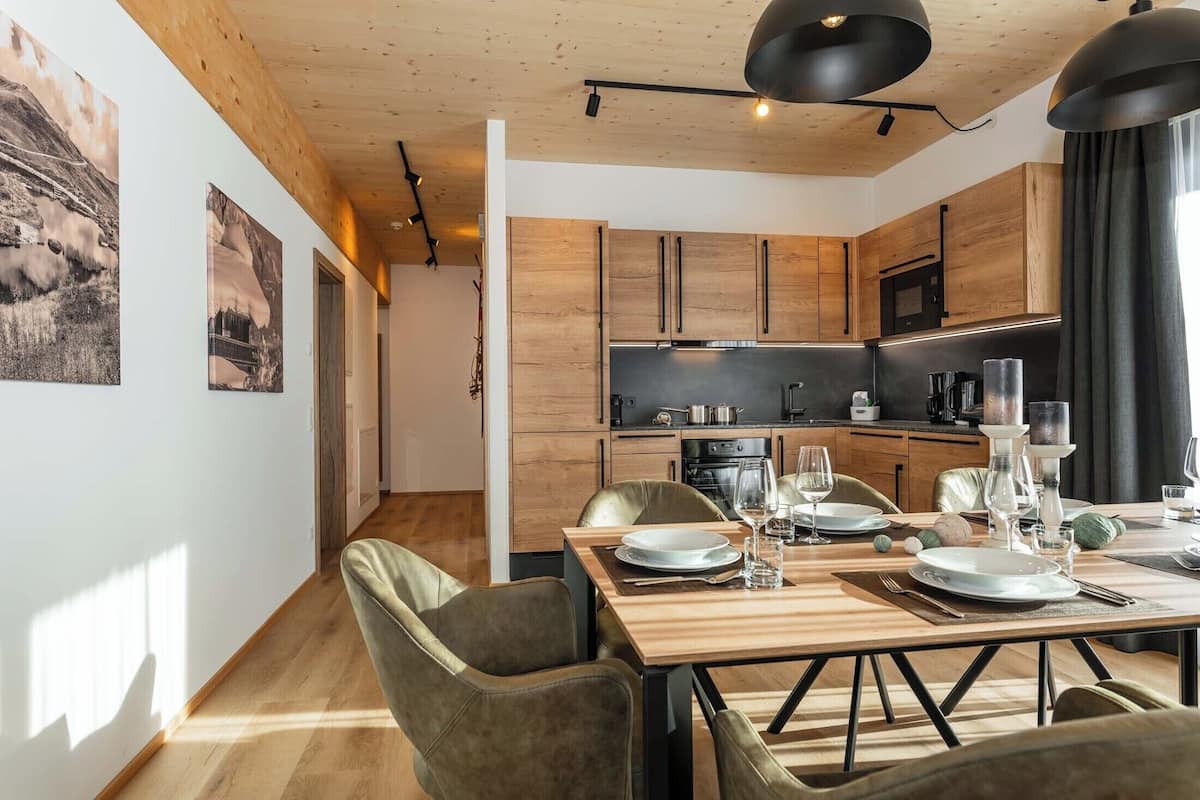 A modern kitchen with wooden cabinets, a dining area with a wooden table and chairs, and a view of the hallway.