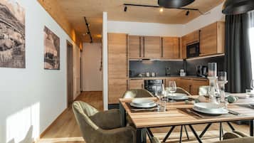 Une cuisine moderne avec des meubles en bois, un coin repas avec une table et des chaises en bois, et une vue sur le couloir.