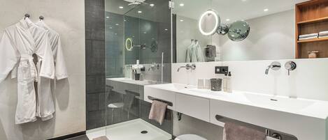 Un baño moderno con dos lavamanos, una cabina de ducha de vidrio y un espejo grande con luz de aro.