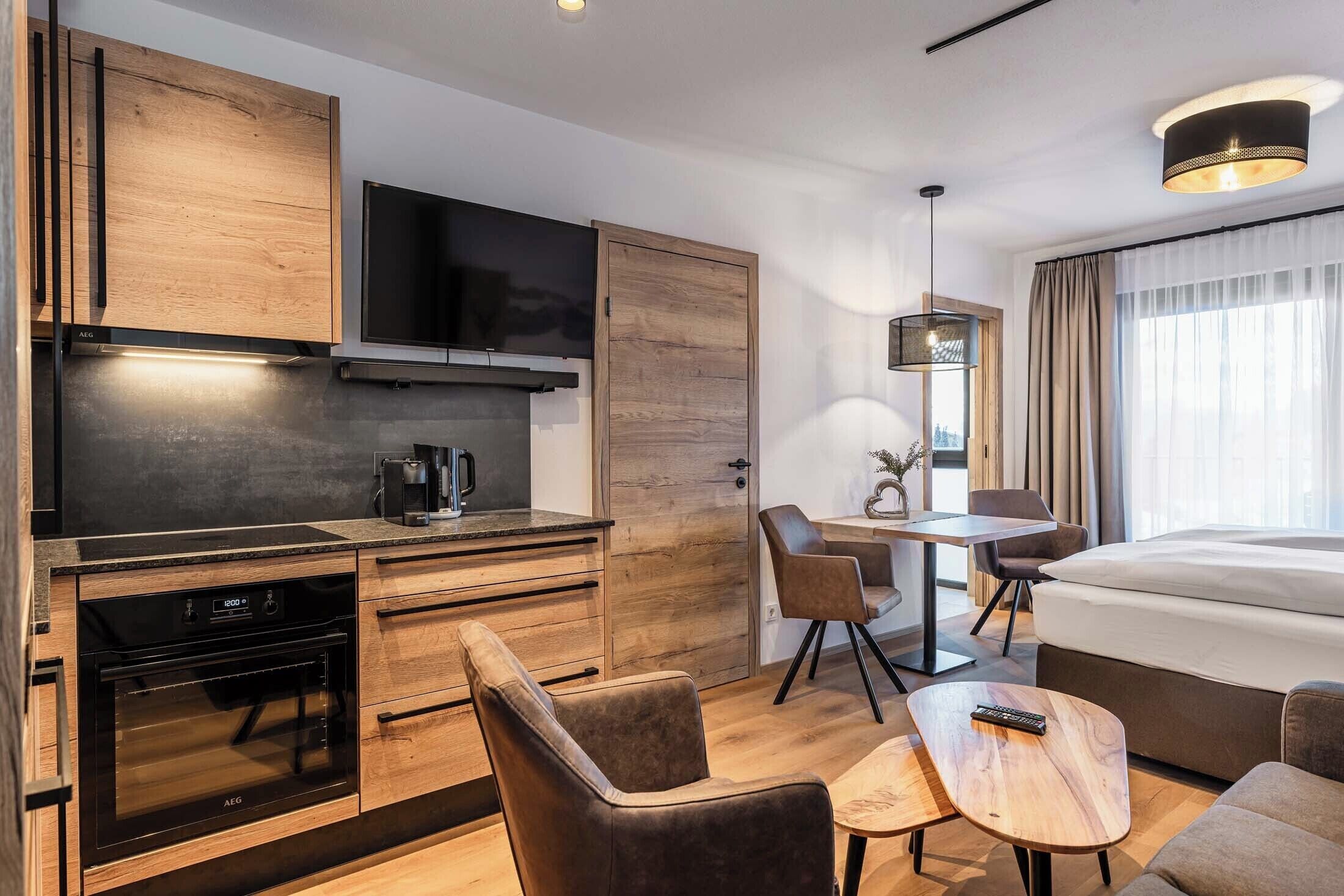Una habitación de hotel moderna con kitchenette, zona de comedor y una cama grande.