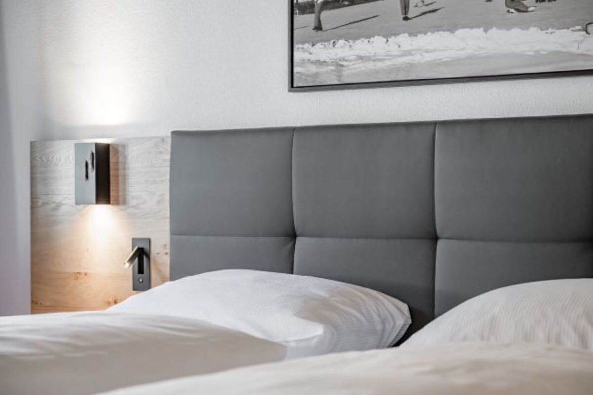 Ett modernt sovrum med en stor säng, en sänggavel och en väggmonterad lampa.