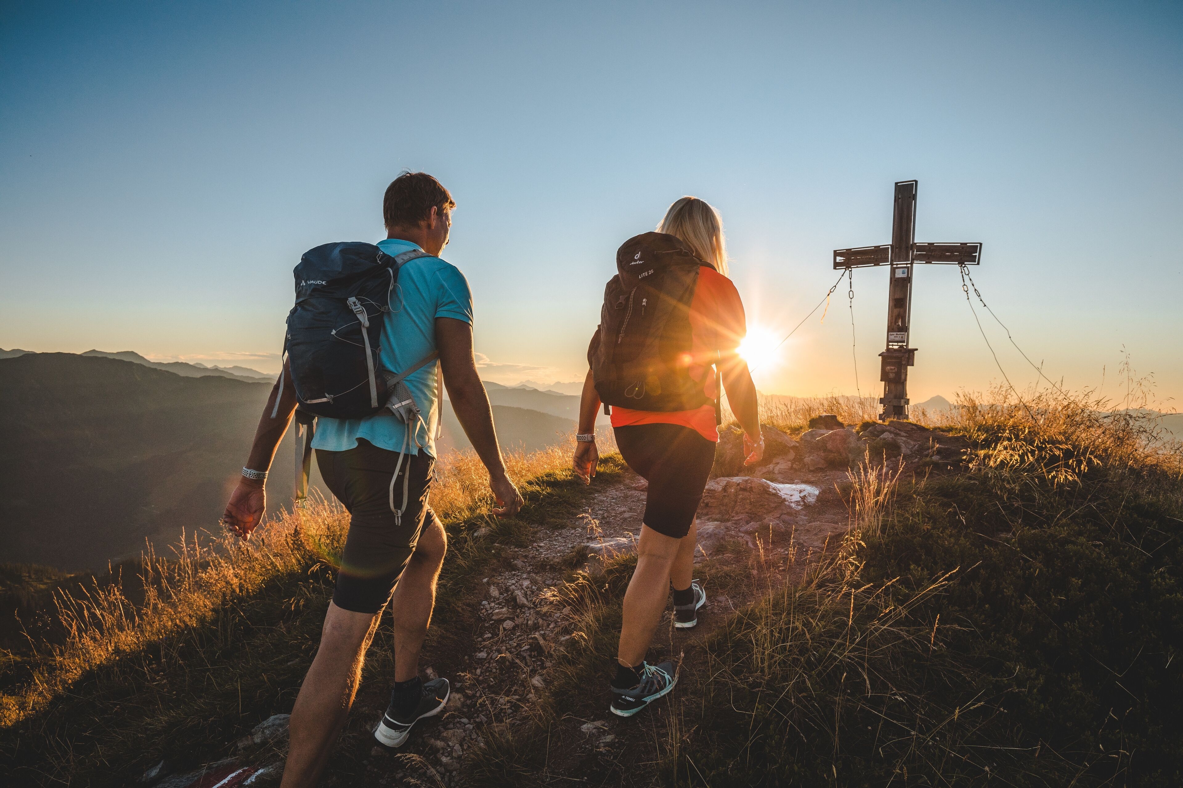 Due escursionisti su un sentiero di montagna, con una croce sullo sfondo.