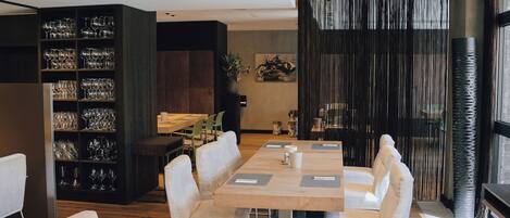 A modern dining area with wooden tables and white chairs, a bookshelf with glassware, and a decorative wall with vertical lines.