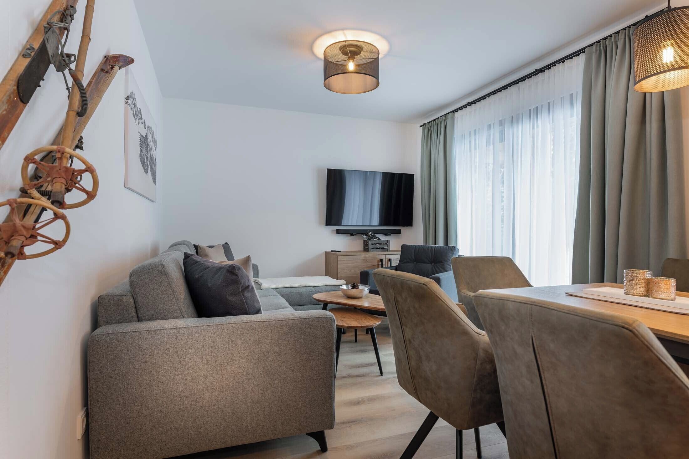 A modern living room with a sofa, chairs, a dining table, and a TV mounted on the wall.