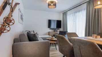 A modern living room with a sofa, chairs, a dining table, and a TV mounted on the wall.