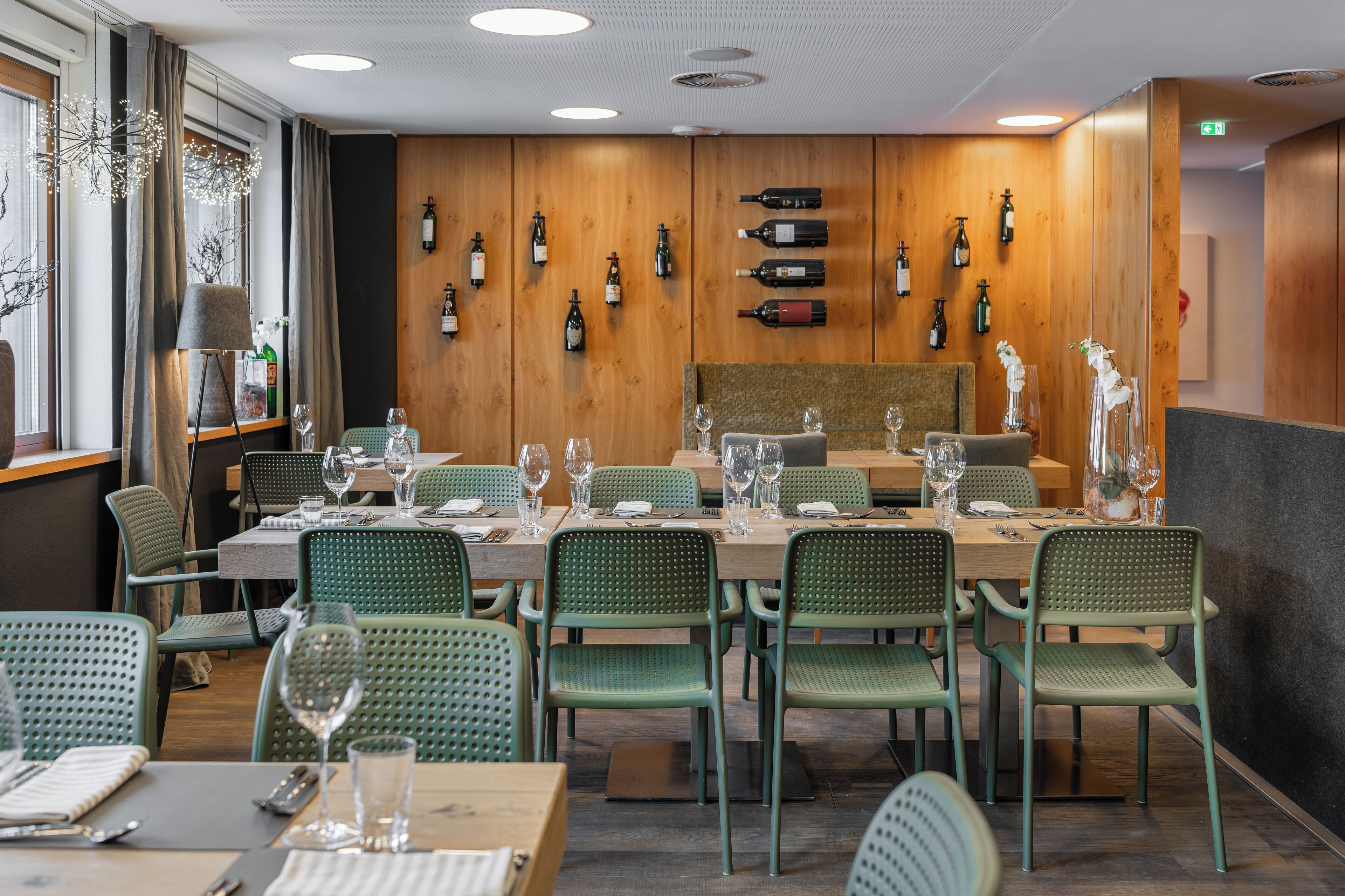 A restaurant with wooden walls, green chairs, and wine bottles displayed on the wall.