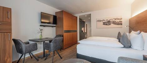 A modern hotel room with a bed, a desk, two chairs, a TV, and a painting on the wall.