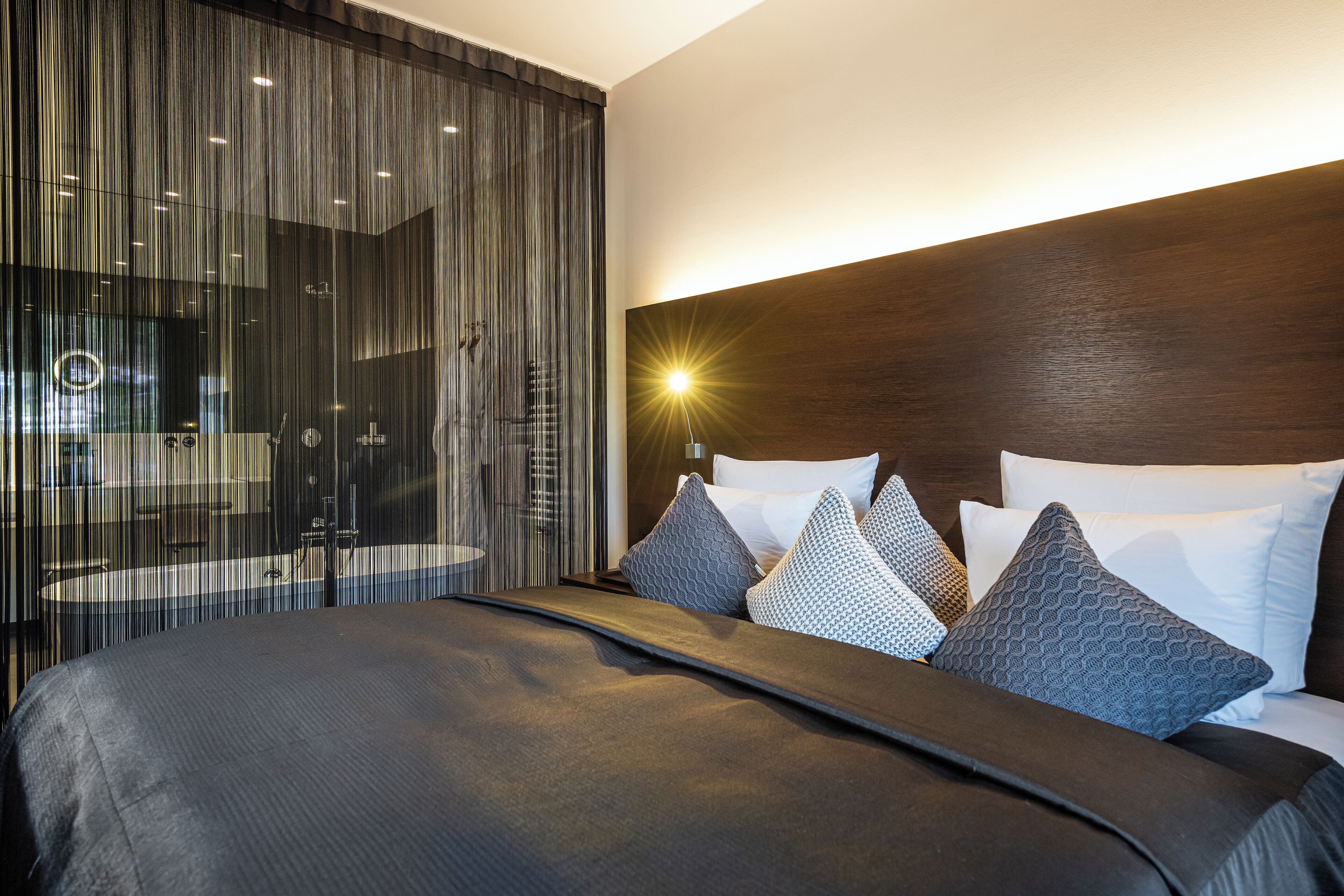A modern hotel room with a large bed, a wooden headboard, and a view of a cityscape through a large window.