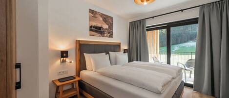A modern bedroom with a large bed, bedside table, and a view of a balcony.