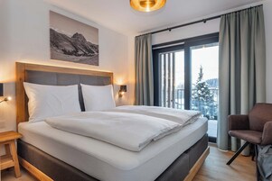 A modern hotel room with a large bed, a nightstand, a chair, and a window with curtains.