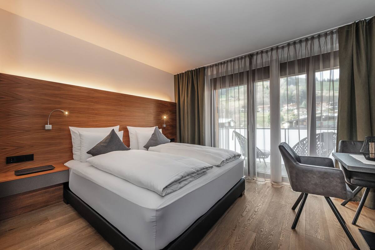A modern hotel room with a large bed, a desk, and a view of a balcony.
