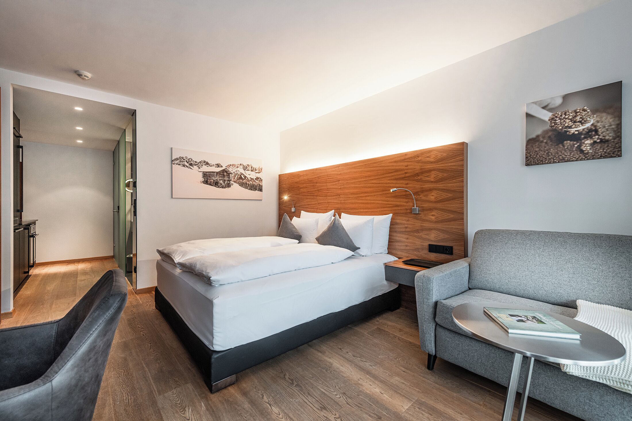 Een moderne hotelkamer met een bed, een grijze bank, een klein tafeltje en een houten hoofdeinde.