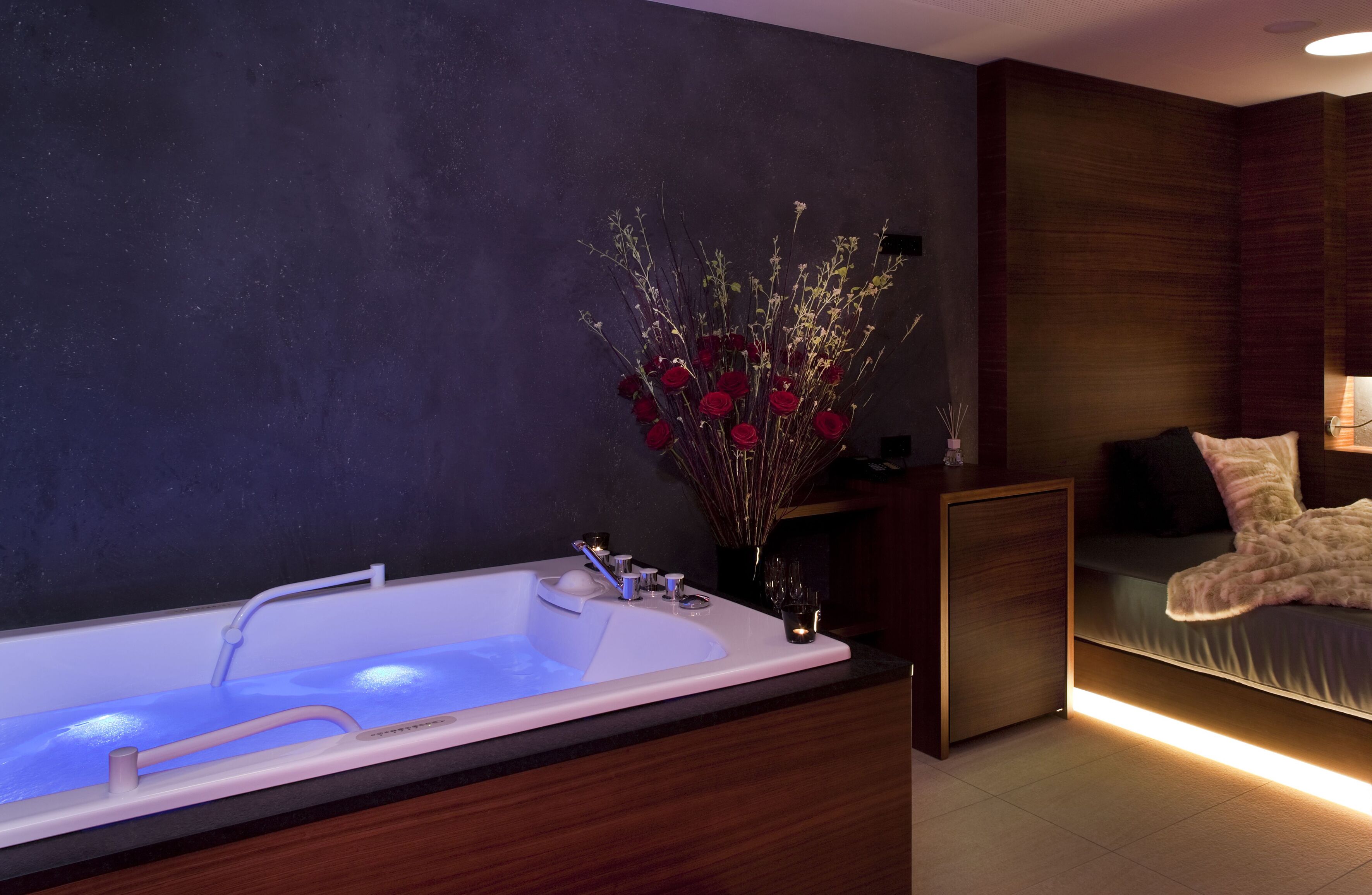 A modern bathroom with a large bathtub, a dark wall, and a wooden vanity.