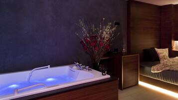 A modern bathroom with a large bathtub, a dark wall, and a wooden vanity.