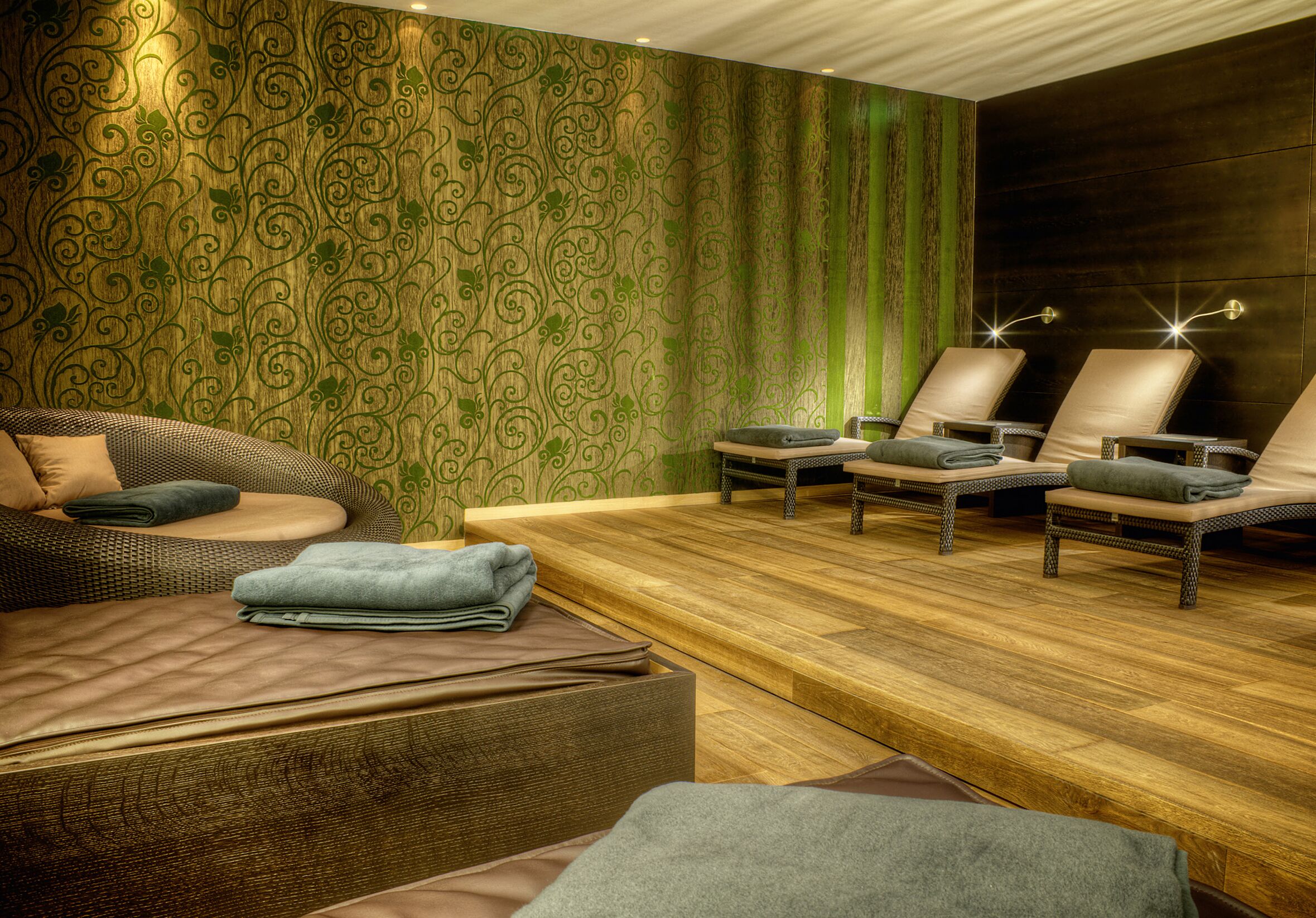 A spa room with a wooden floor, a massage table, and two massage chairs.