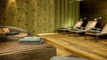 A spa room with a wooden floor, a massage table, and two massage chairs.