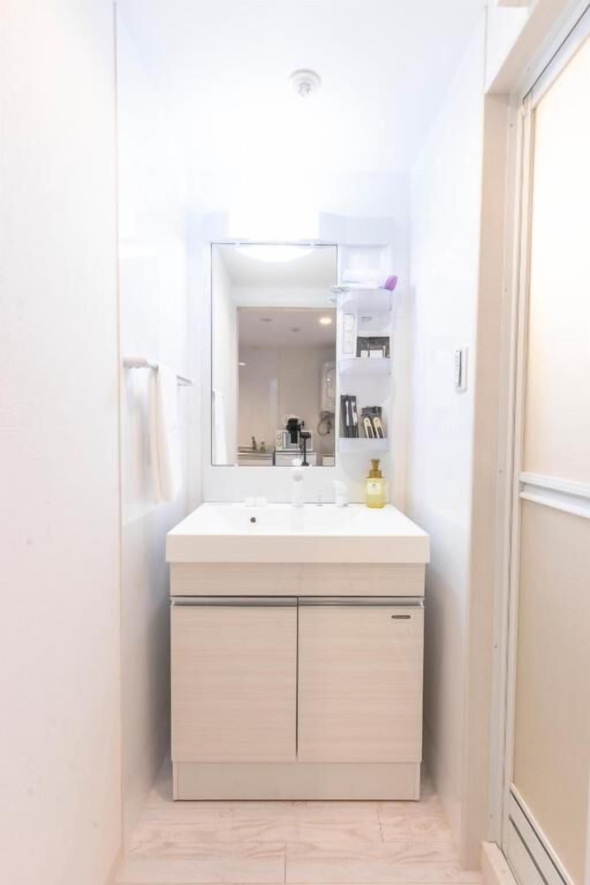 A narrow bathroom with a white vanity, a mirror, and a shelf with toiletries.
