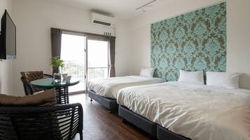 A hotel room with two beds, a balcony with curtains, a small table with a plant, and a TV mounted on the wall.