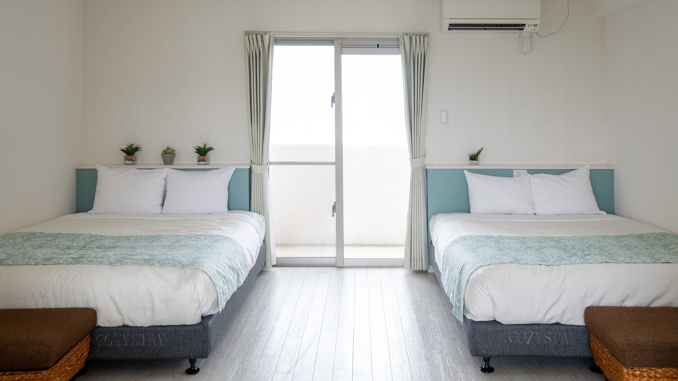 Een hotelkamer met twee bedden, een schuifdeur en een kleine potplant op elk bed.