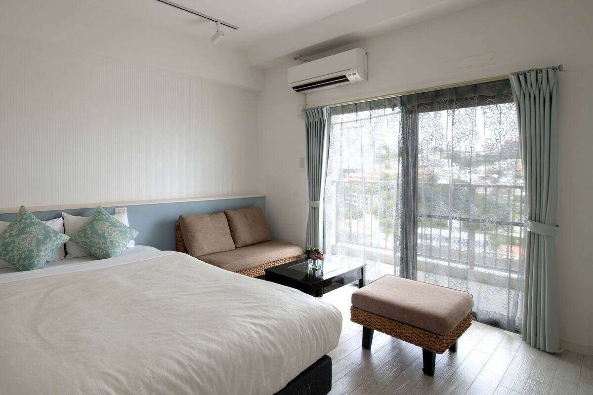 A hotel room with a large bed, a sofa, a small table, and a window with curtains.