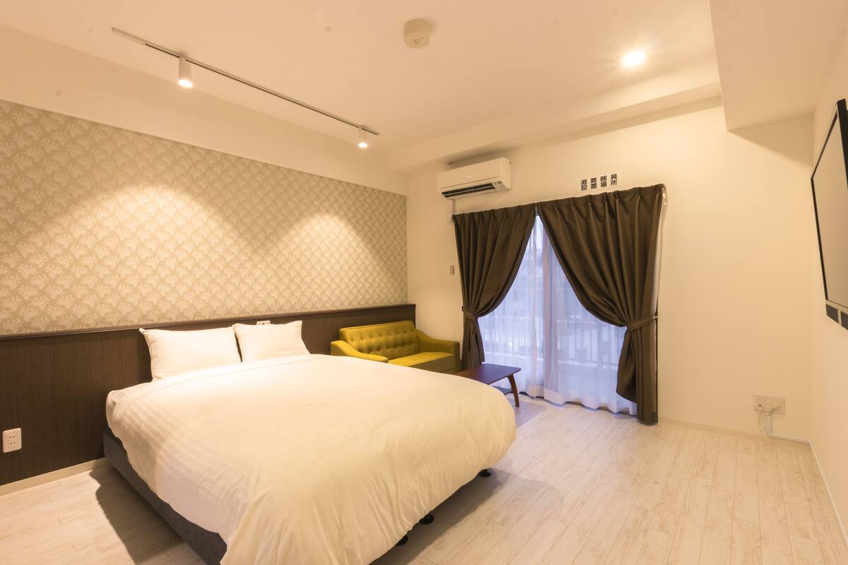 A hotel room with a large bed, a sofa, a small table, and a window with curtains.