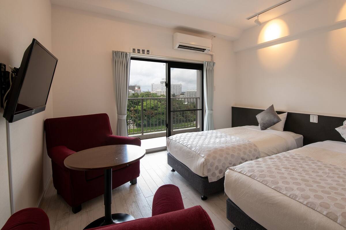 A hotel room with two beds, a TV, a red chair, and a table.