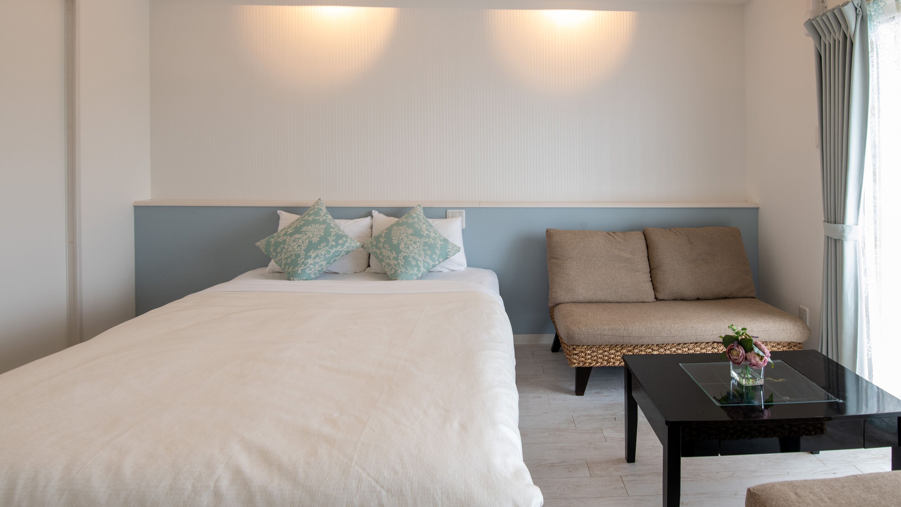 A hotel room with a bed, a sofa, a small table, and a window with curtains.
